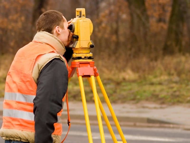 Professional land surveyor using a total station to measure property boundaries in the field