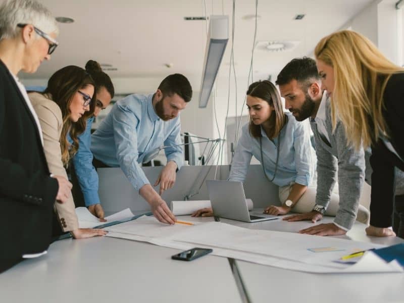 Team of professionals reviewing ALTA survey plans on a table during a commercial property planning meeting for investment and site analysis decisions.