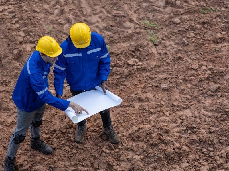Two construction professionals reviewing a blueprint on a dirt site during early-stage ALTA survey planning for commercial development.